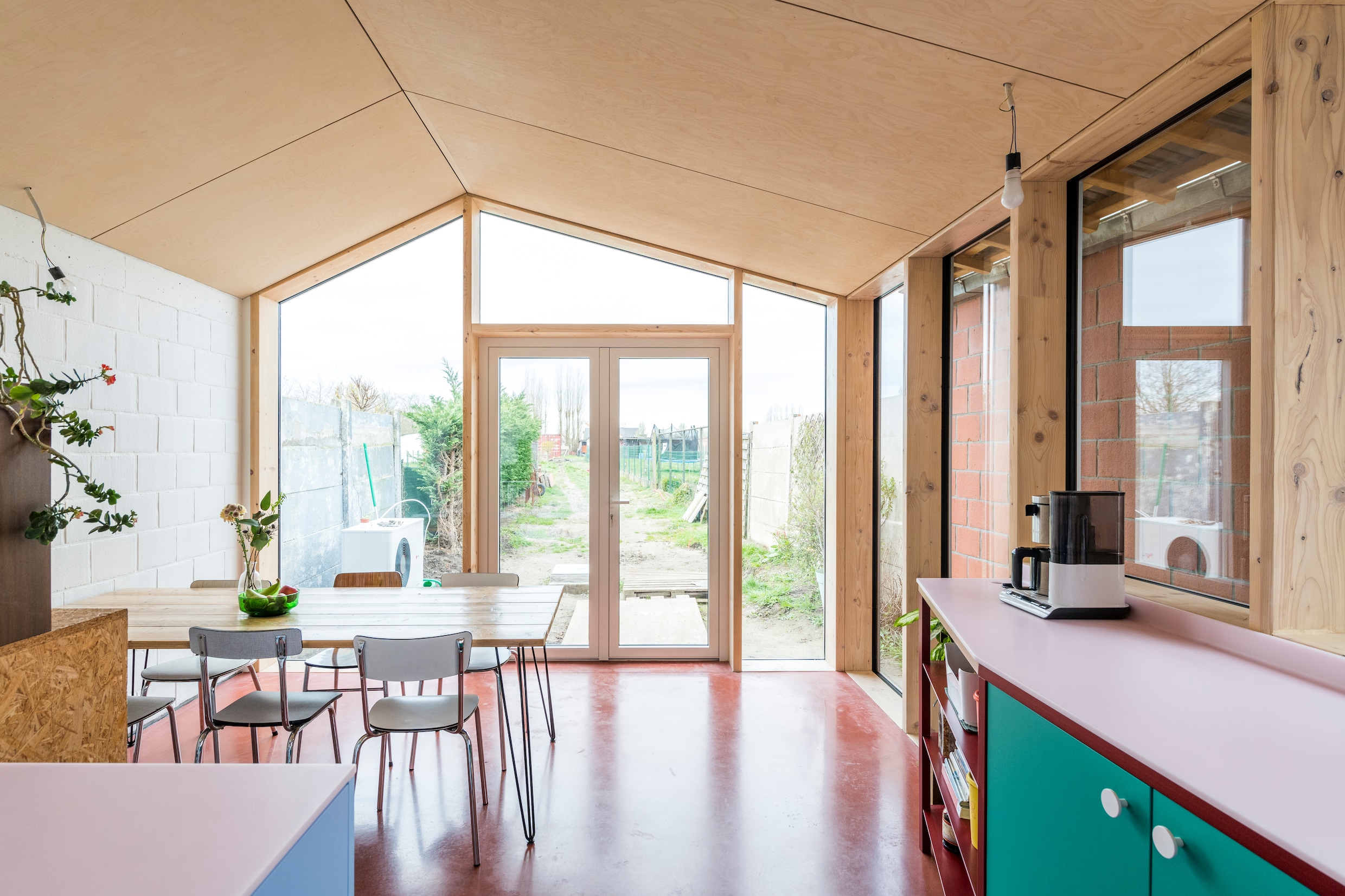 De uitbouw is opgevat als een huisje met puntdak, dat het gevoel van ruimtelijkheid ­vergroot. Door de glazen zijgevel is de groene achterkant van het keukenmeubel zichtbaar langs de buitenkant.