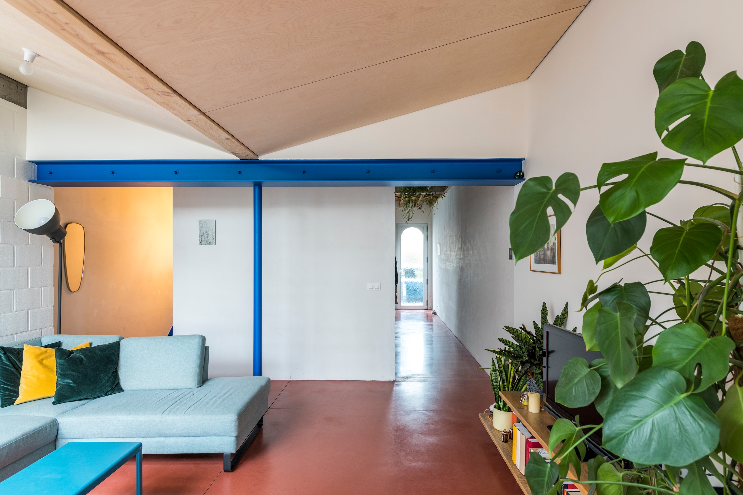 De blauwe steunbalk markeert de grens tussen het oude huis en de nieuwe uitbouw. De trap zit ‘ingepakt’ in het volume achter de zithoek.